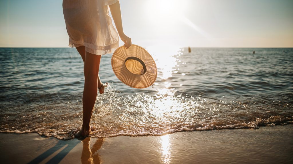 woman walking along the beach holding her straw-hat