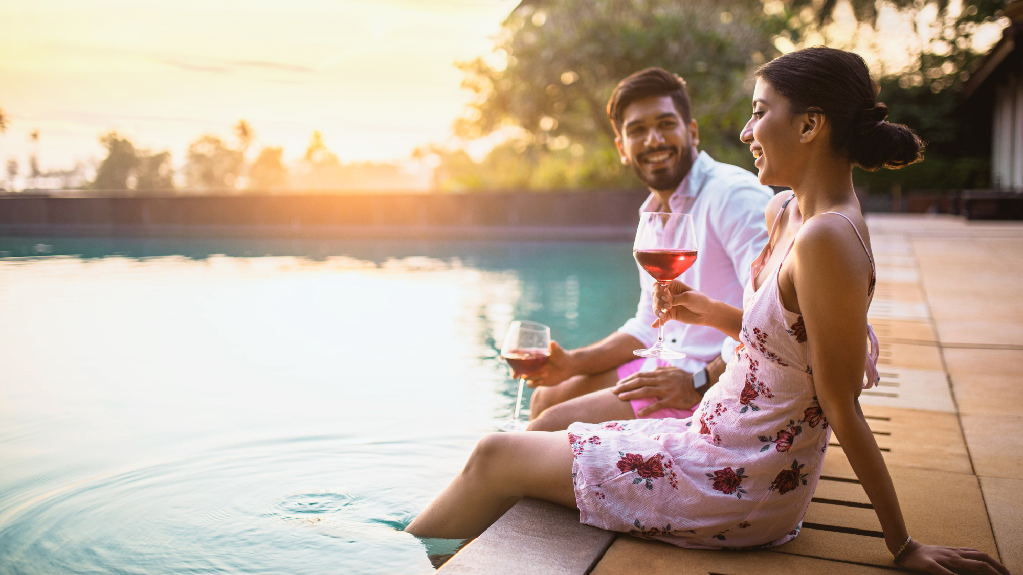 two people sitting on edge of pool drinking wine