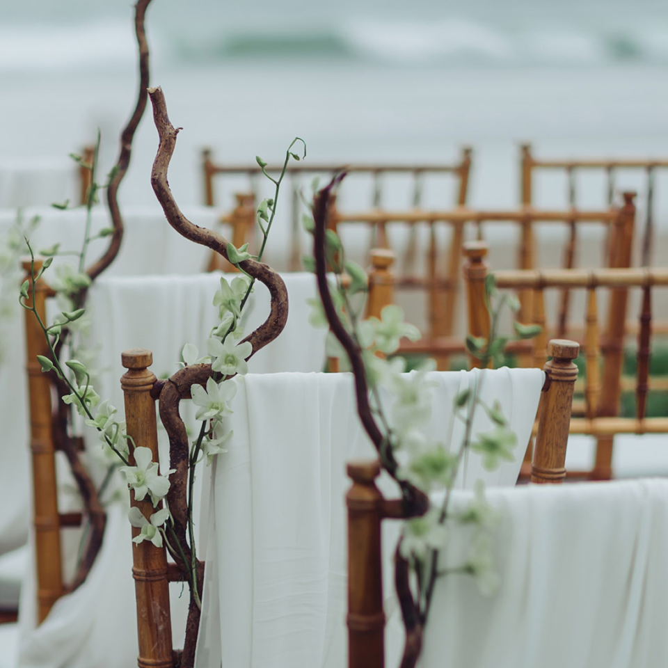 Wooden chairs wrapped in white flowers and white drapes for a wedding ceremony
