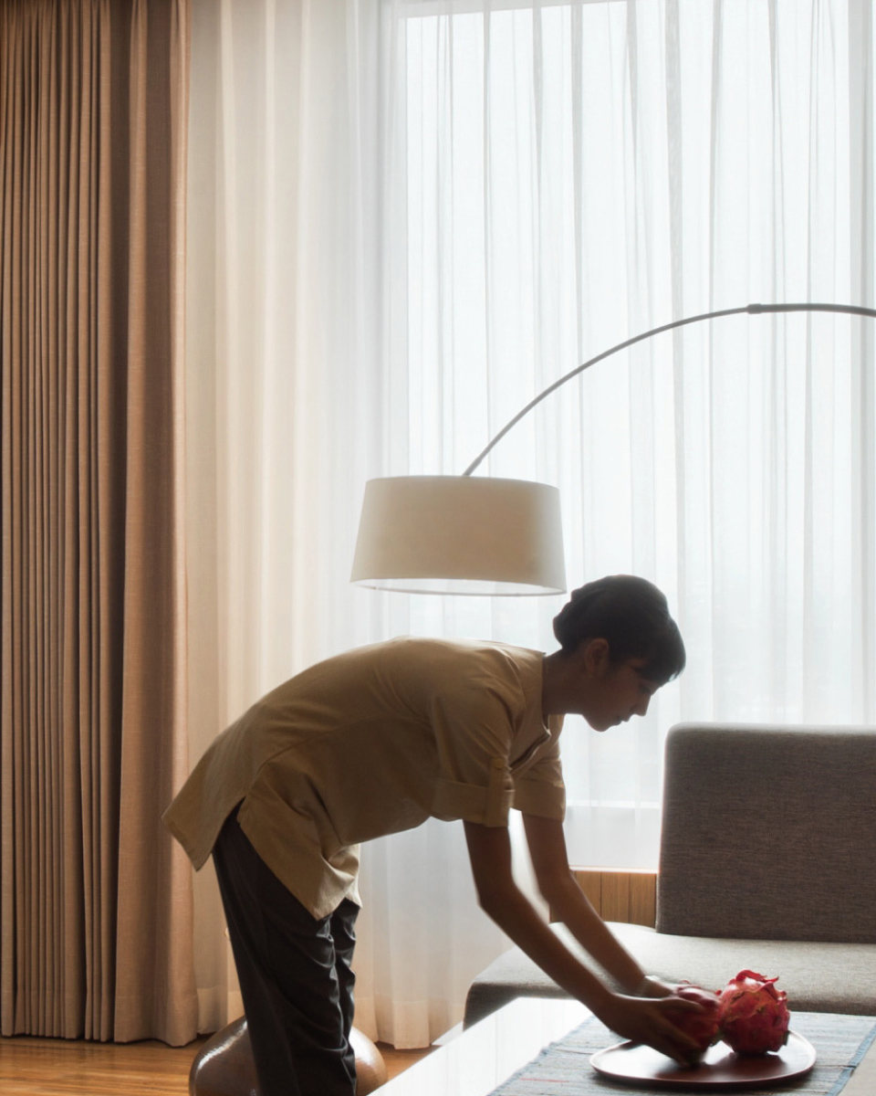 hotel staff places a fruitbowl on a table in a hotel room