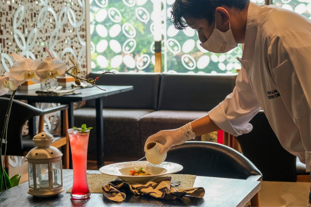 Chef table side pouring sauce on a plated dish